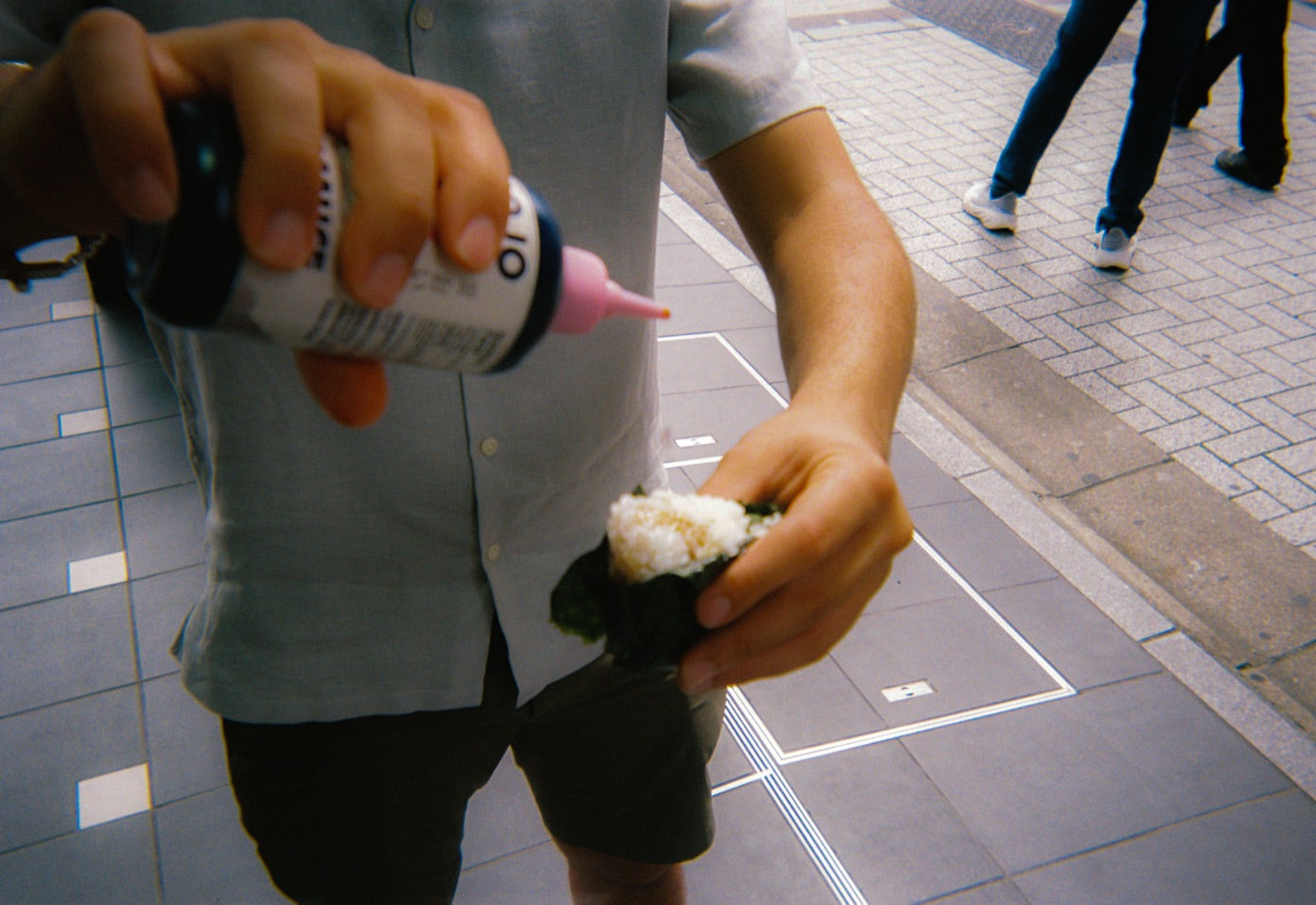 Squeezing Dojo soy sauce onto an onigiri on a Tokyo sidewalk