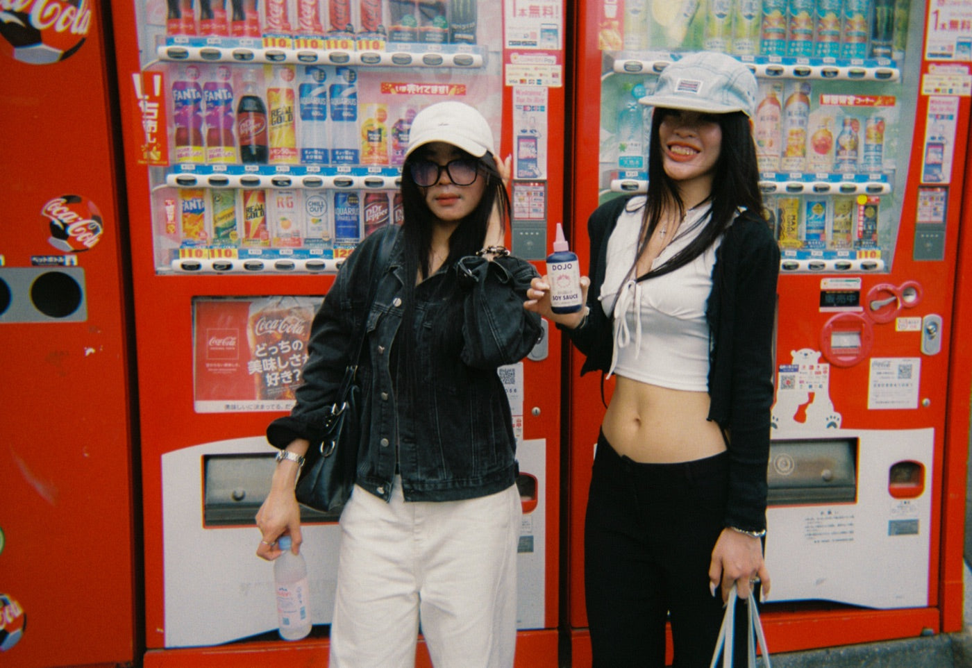 Two friends posing with the bottle at a row of red vending machines