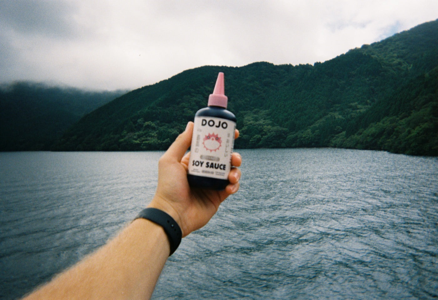 The Dojo bottle held up on 35mm film against a lake and the forested mountains it comes from