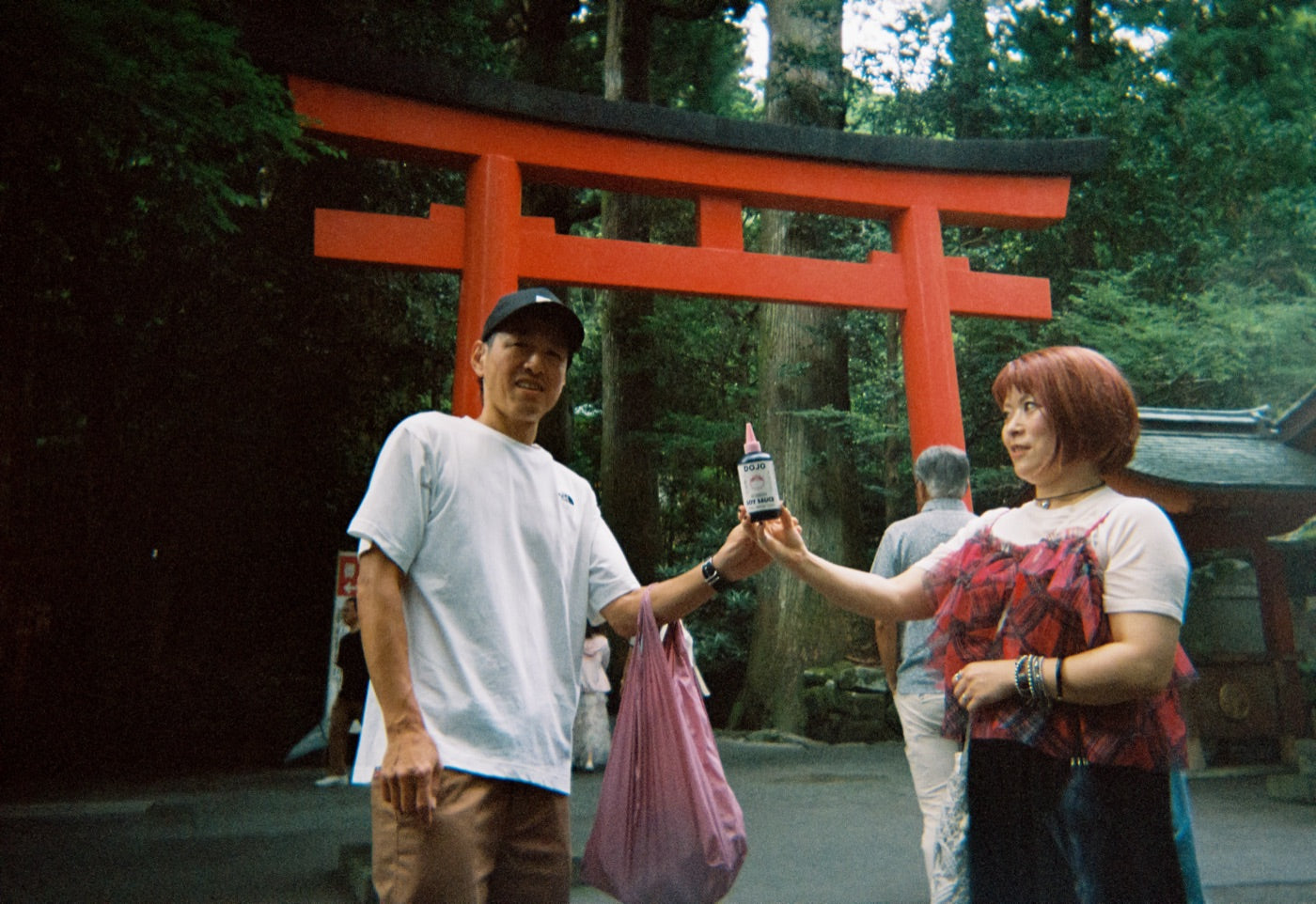 Handing the bottle over in front of a red torii gate
