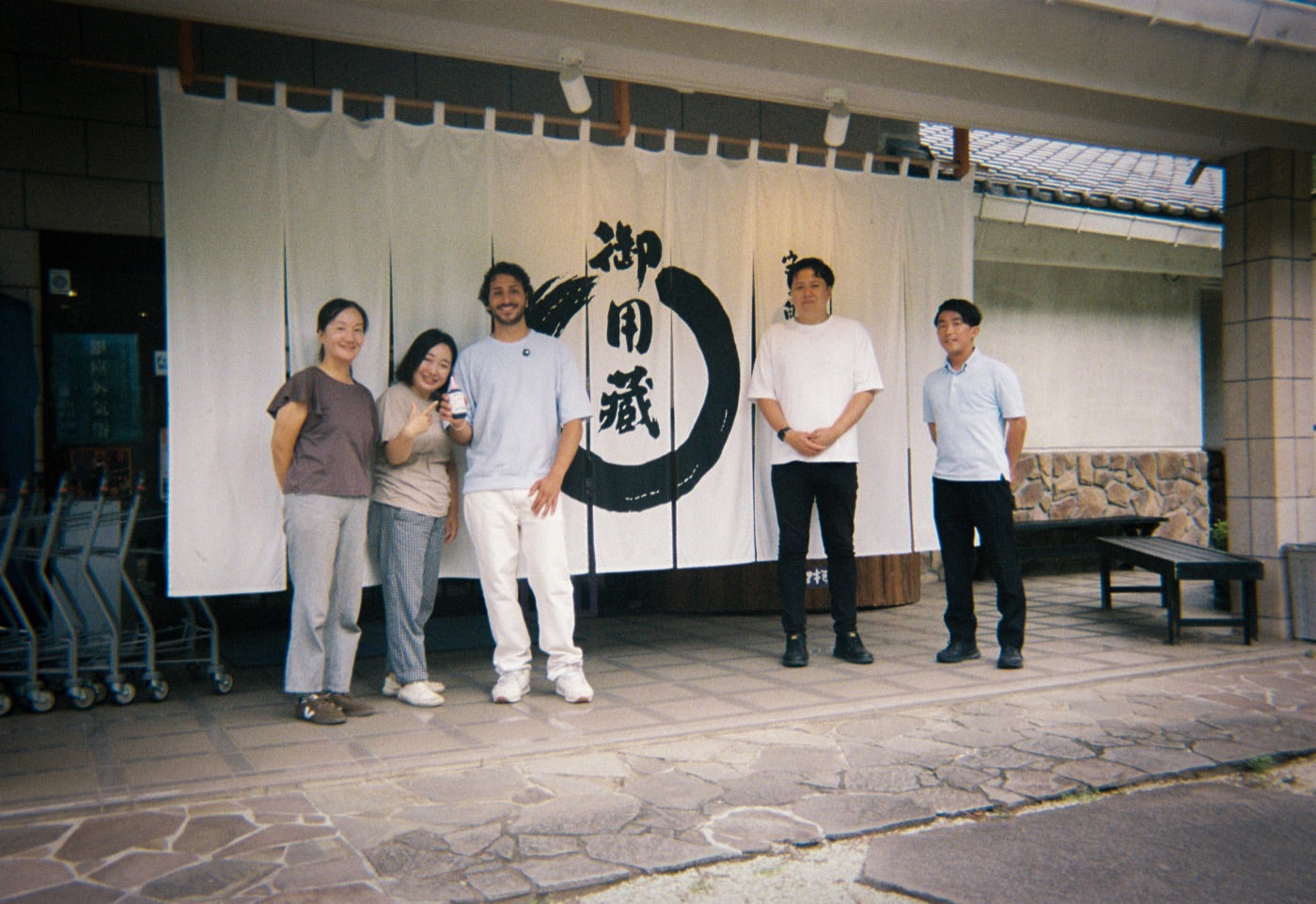 The family and the Dojo crew standing under the brewery's calligraphy noren, on 35mm film