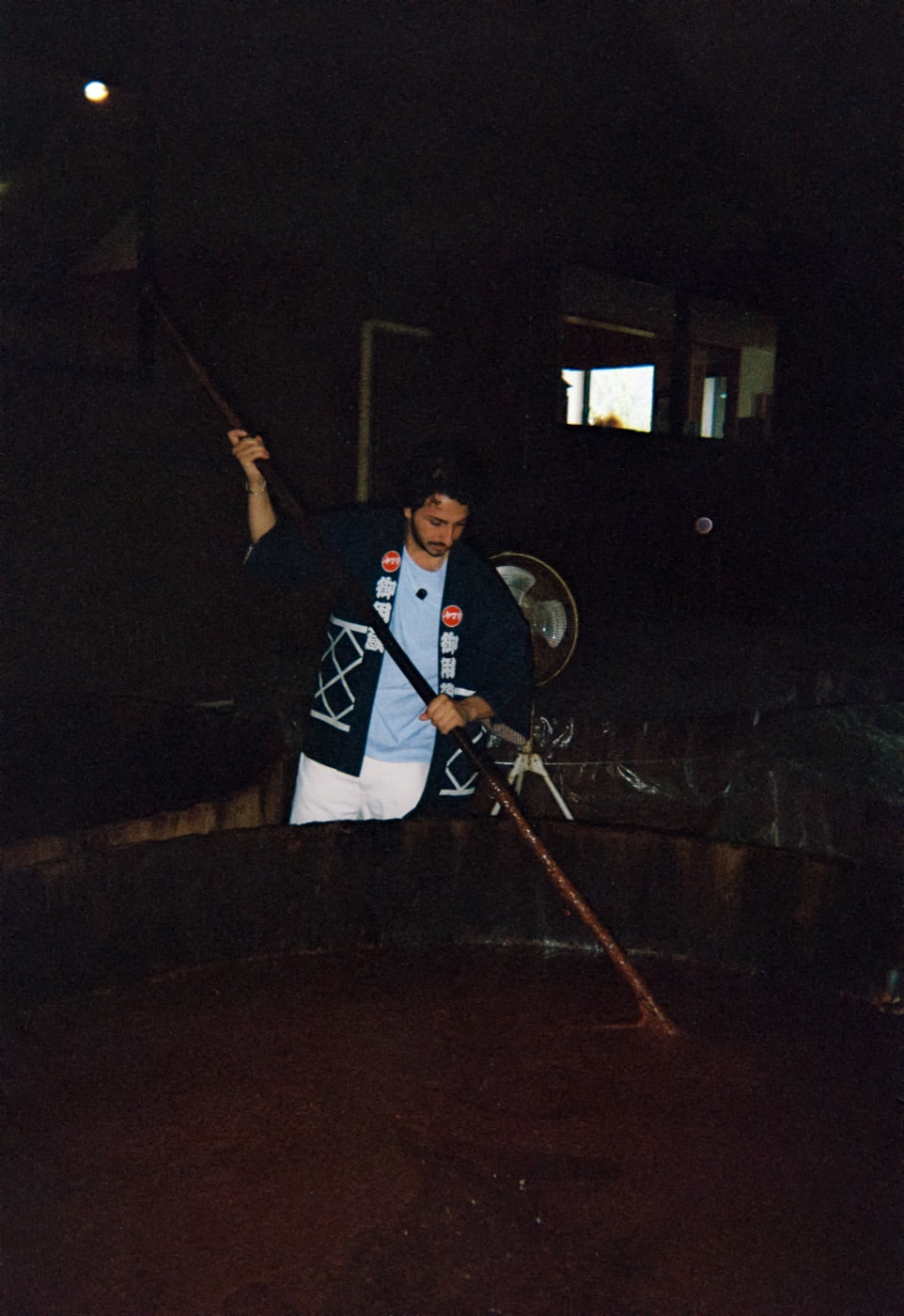 Chaz in a brewer's happi coat, stirring a cedar vat of moromi with a long wooden pole