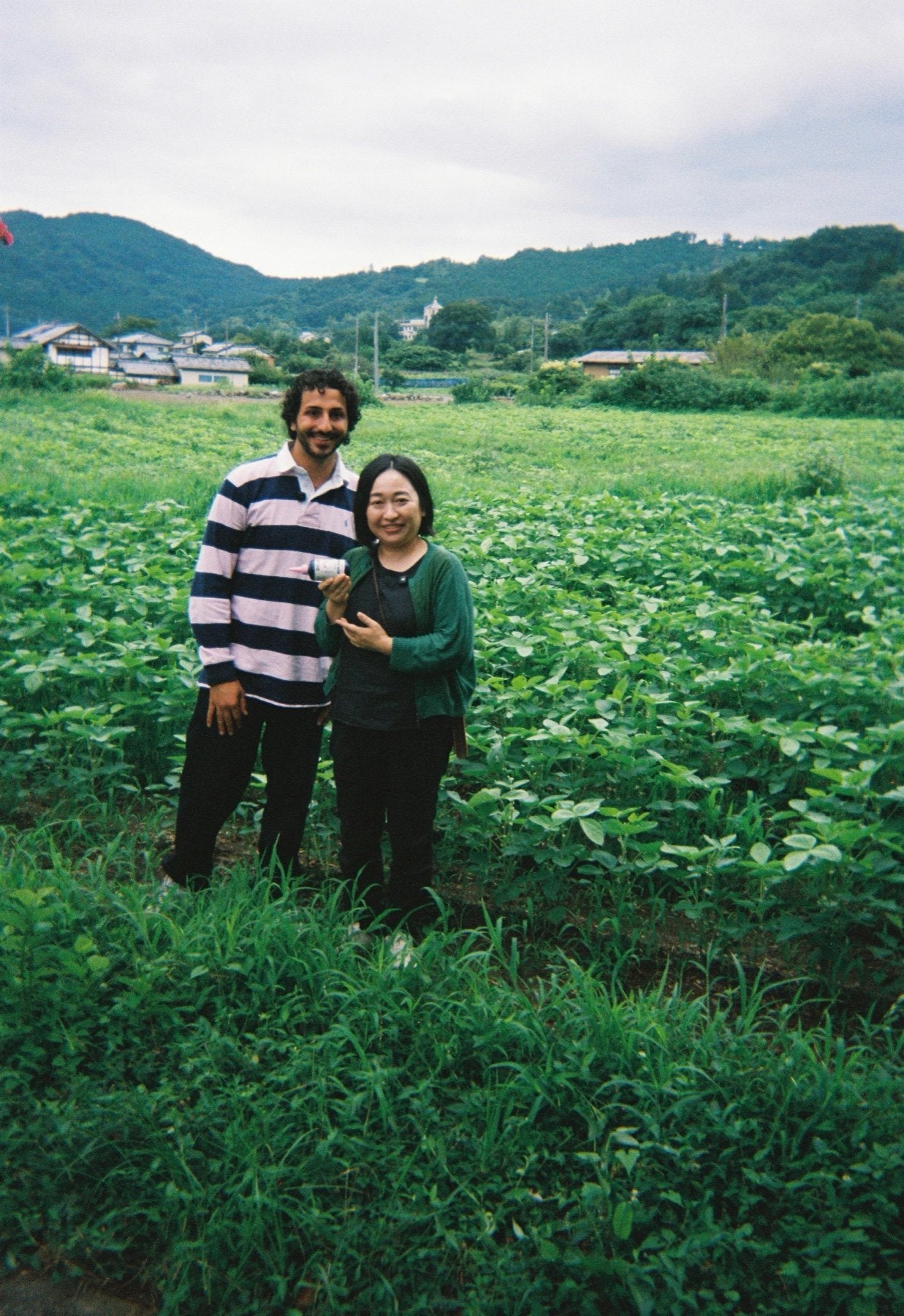 Mami and Charles standing together in a soybean field below the brewery's mountains