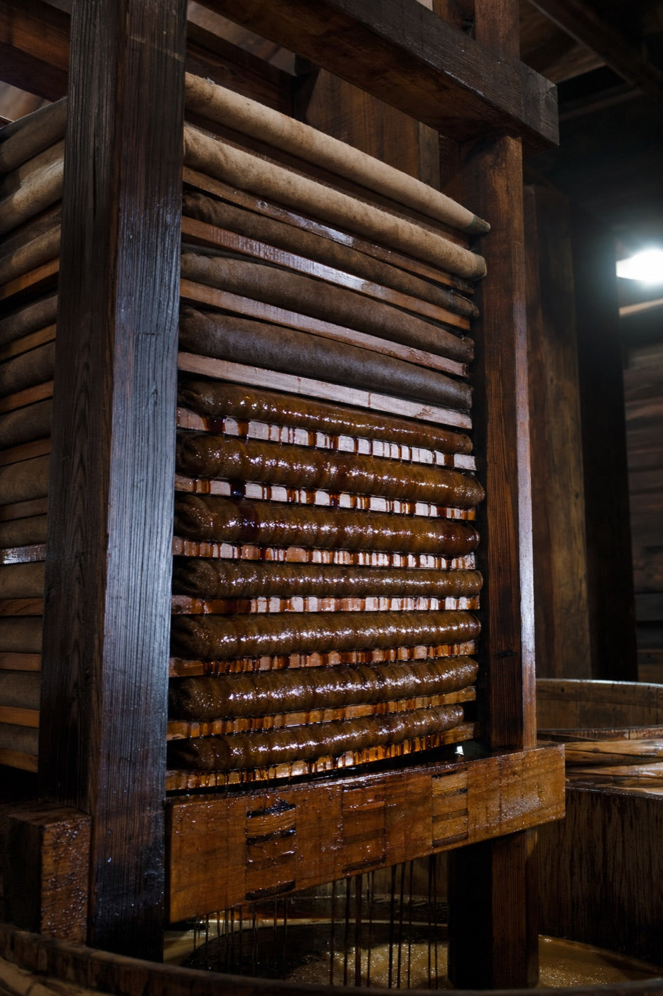 Dark raw soy sauce dripping from cloth-wrapped layers of moromi in a wooden fune press