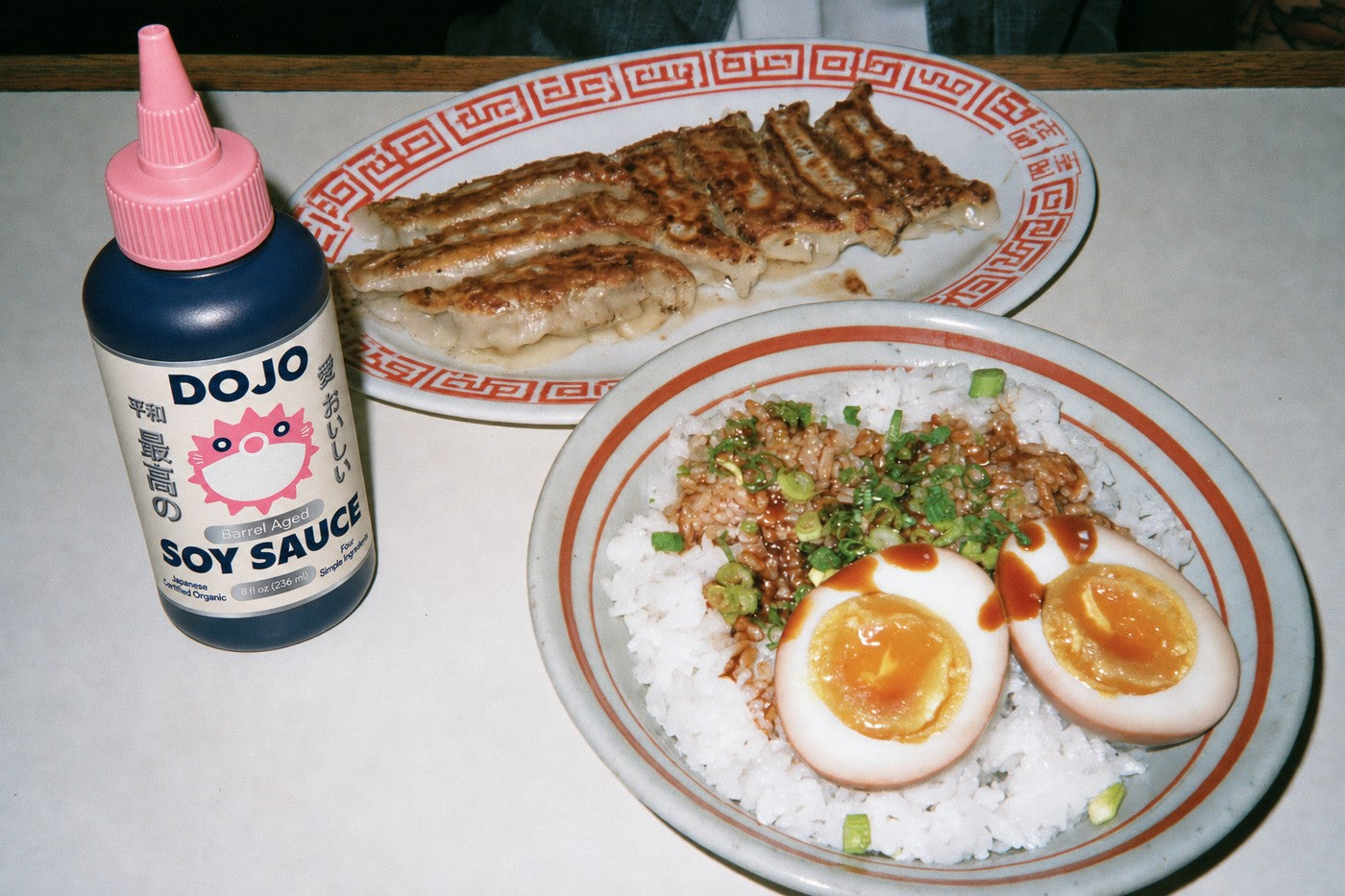 The Dojo bottle standing beside a bowl of rice with jammy soy eggs and a plate of gyoza
