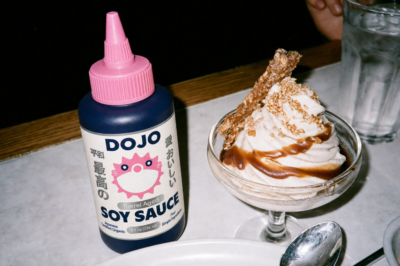 The Dojo bottle standing beside a coupe of vanilla soft serve with a soy caramel ribbon and sesame