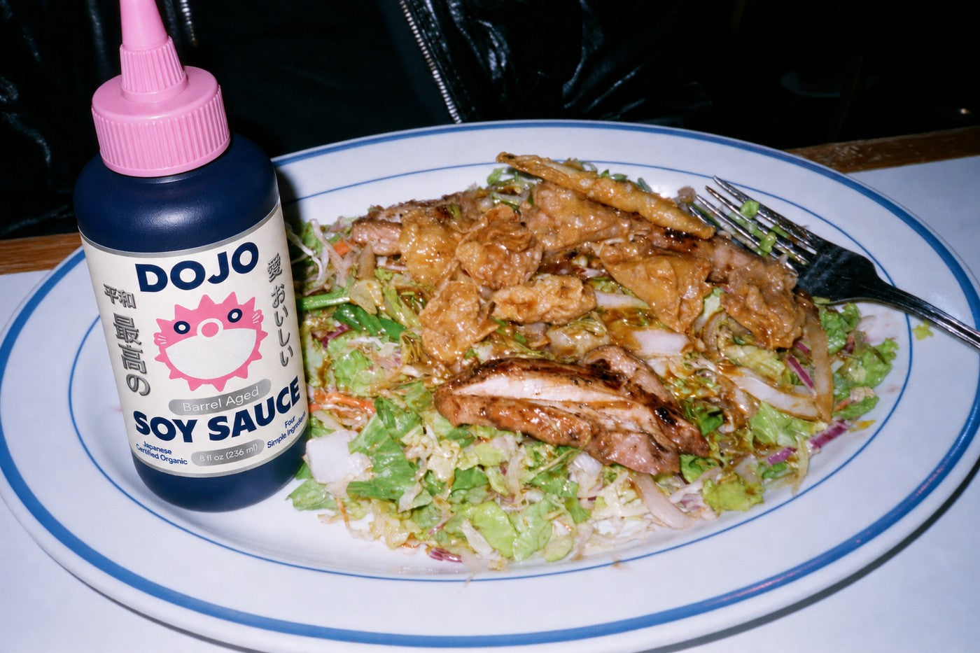 The Dojo bottle standing beside a crunchy chopped salad with grilled chicken and crispy wontons