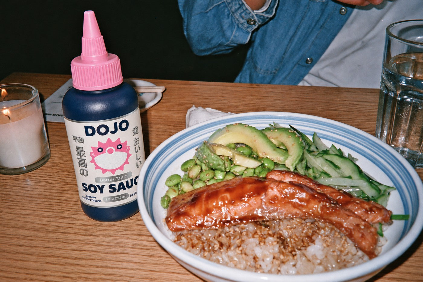 The Dojo bottle standing beside a glazed salmon rice bowl with avocado and edamame