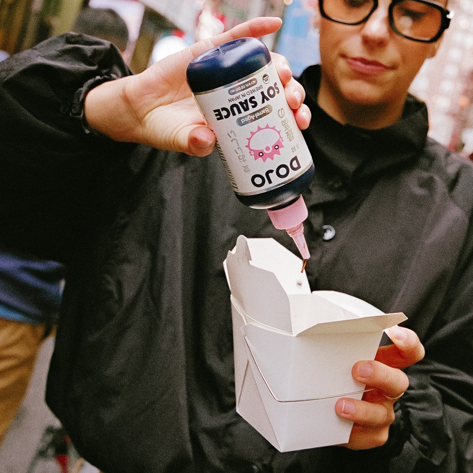 Squeezing DOJO soy sauce into a takeout box on a city street